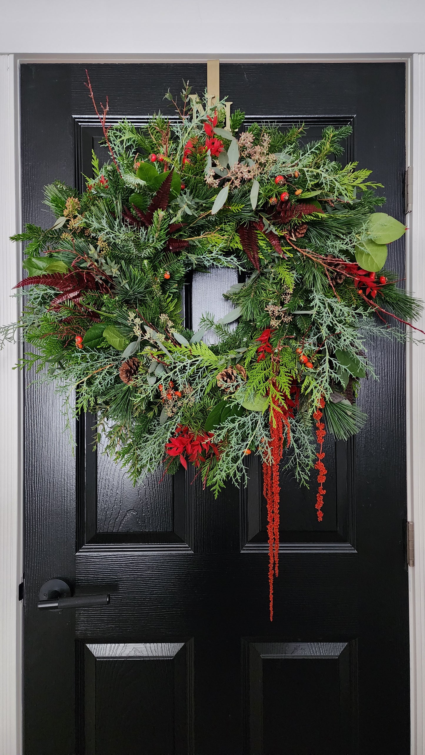 Decorative wreath with greenery and red berries on a black door.