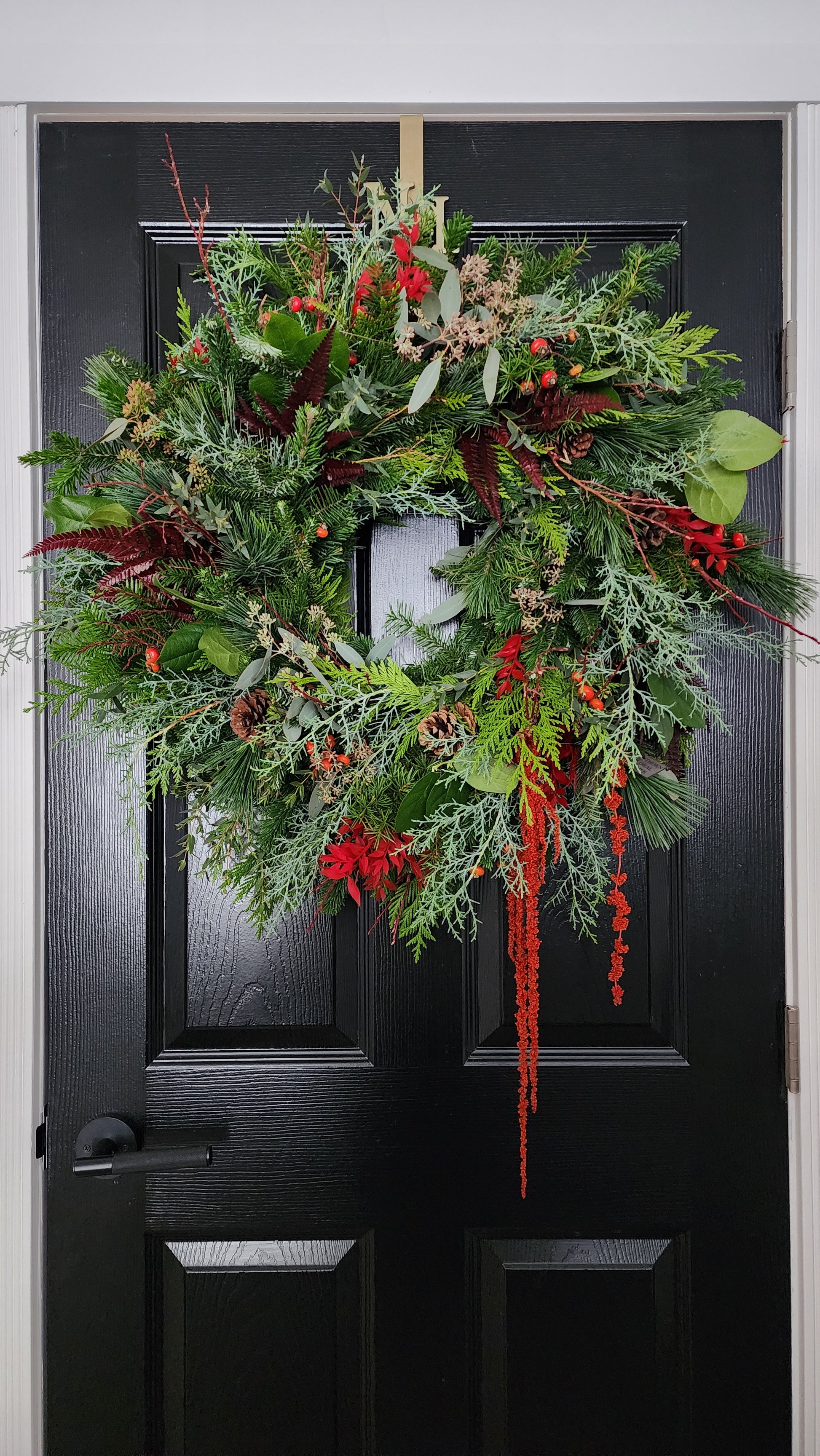 Decorative wreath with greenery and red berries on a black door.
