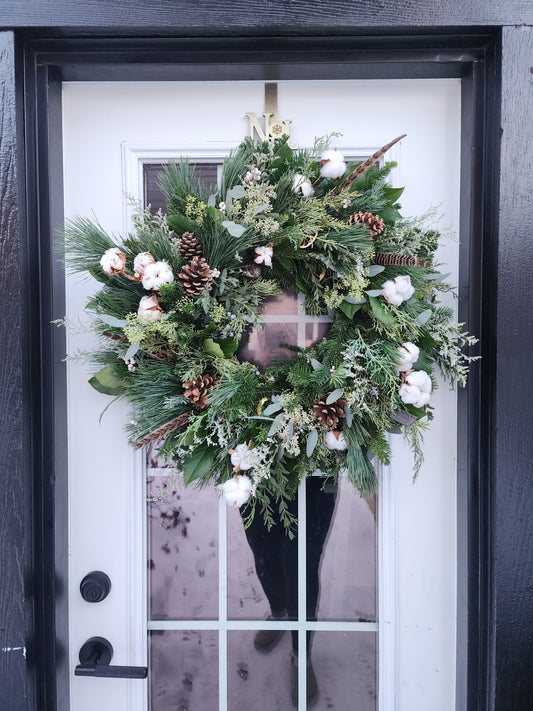 Decorative wreath with greenery, pinecones, and white flowers on a door.