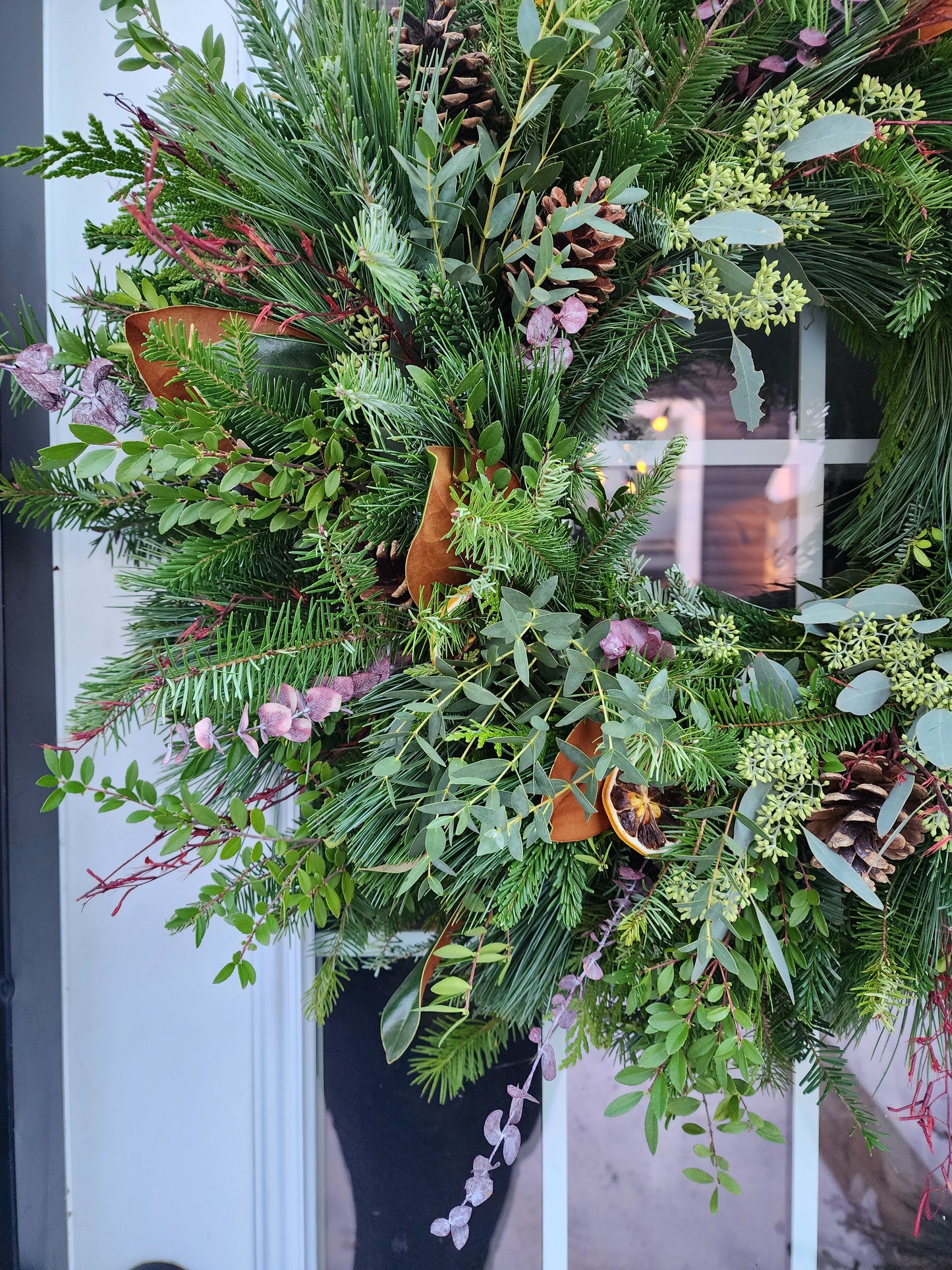 Decorative wreath with greenery and pinecones on a door