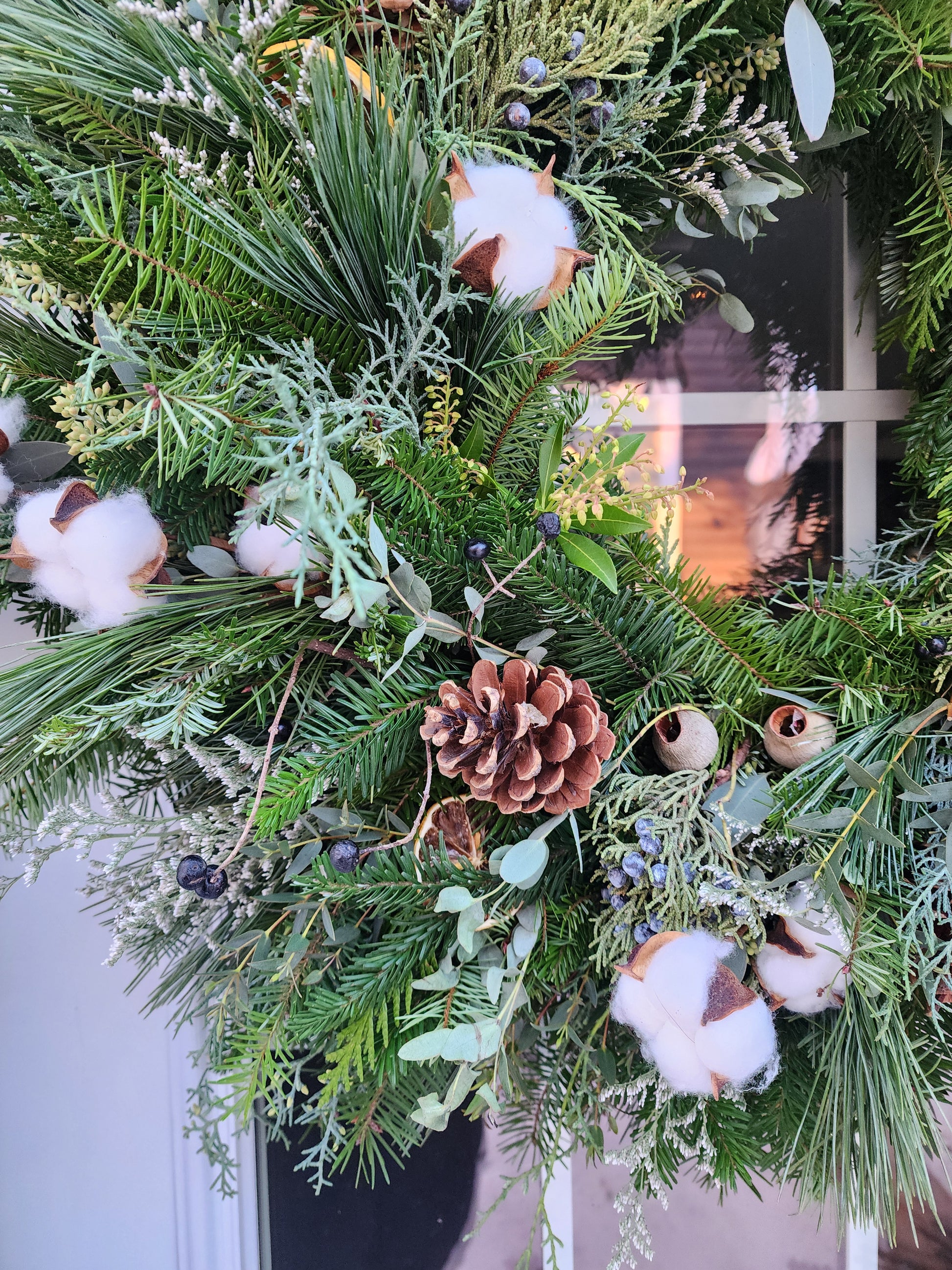 Decorative wreath with greenery, cotton, pinecones, and berries on a door.