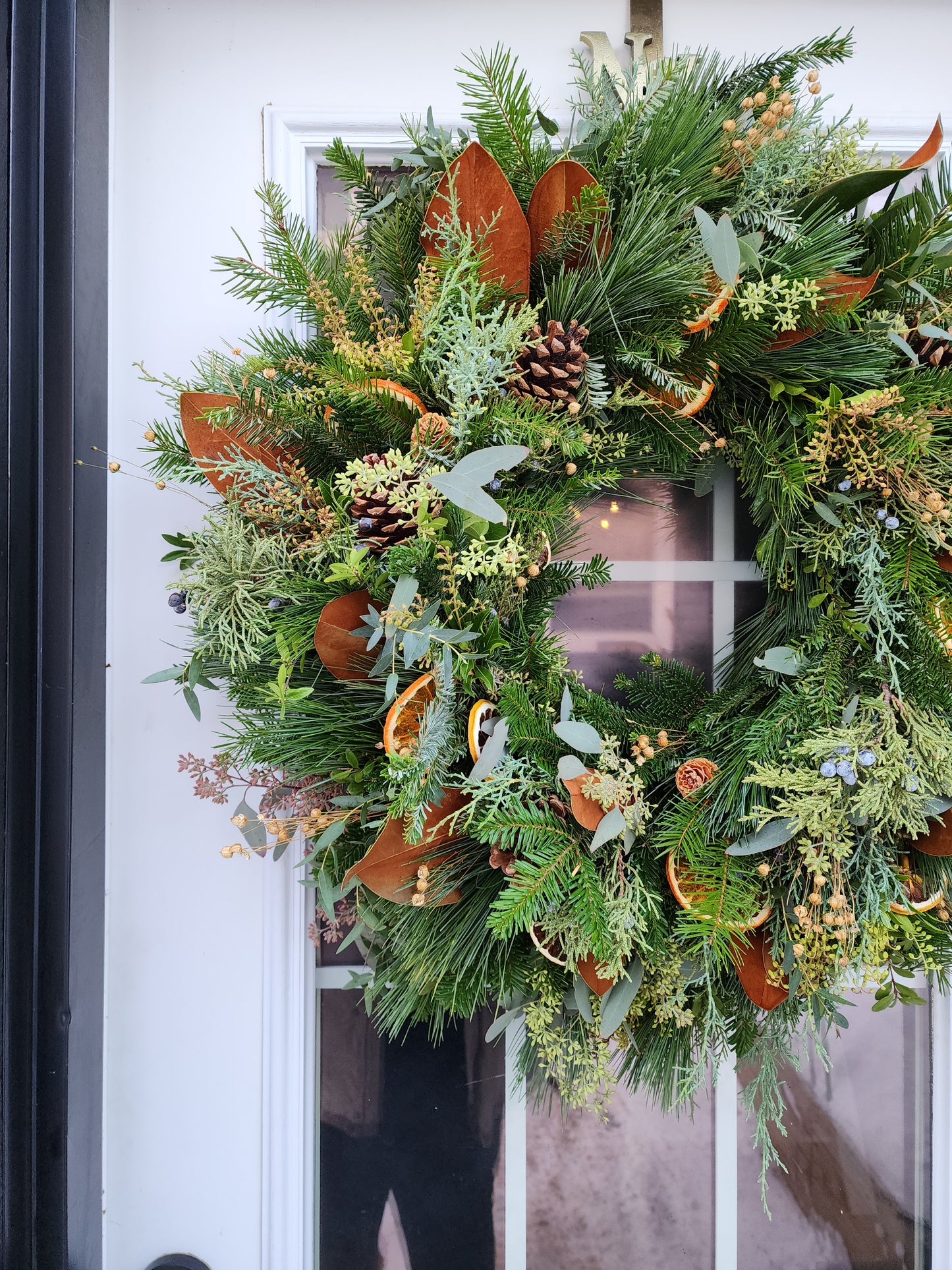 Decorative wreath with greenery, oranges, and pinecones on a door.