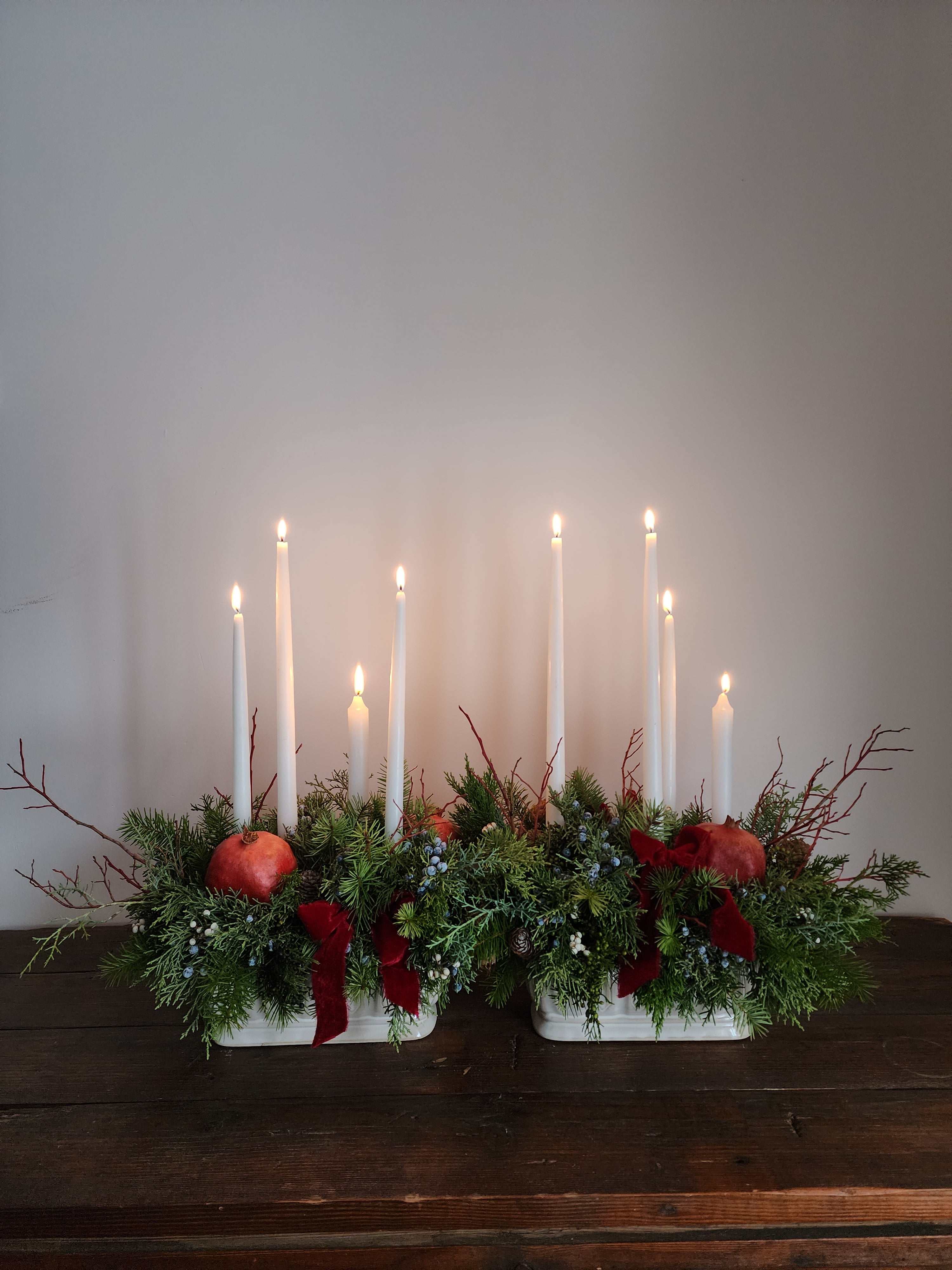 Decorative arrangement with candles and greenery on a white wall.