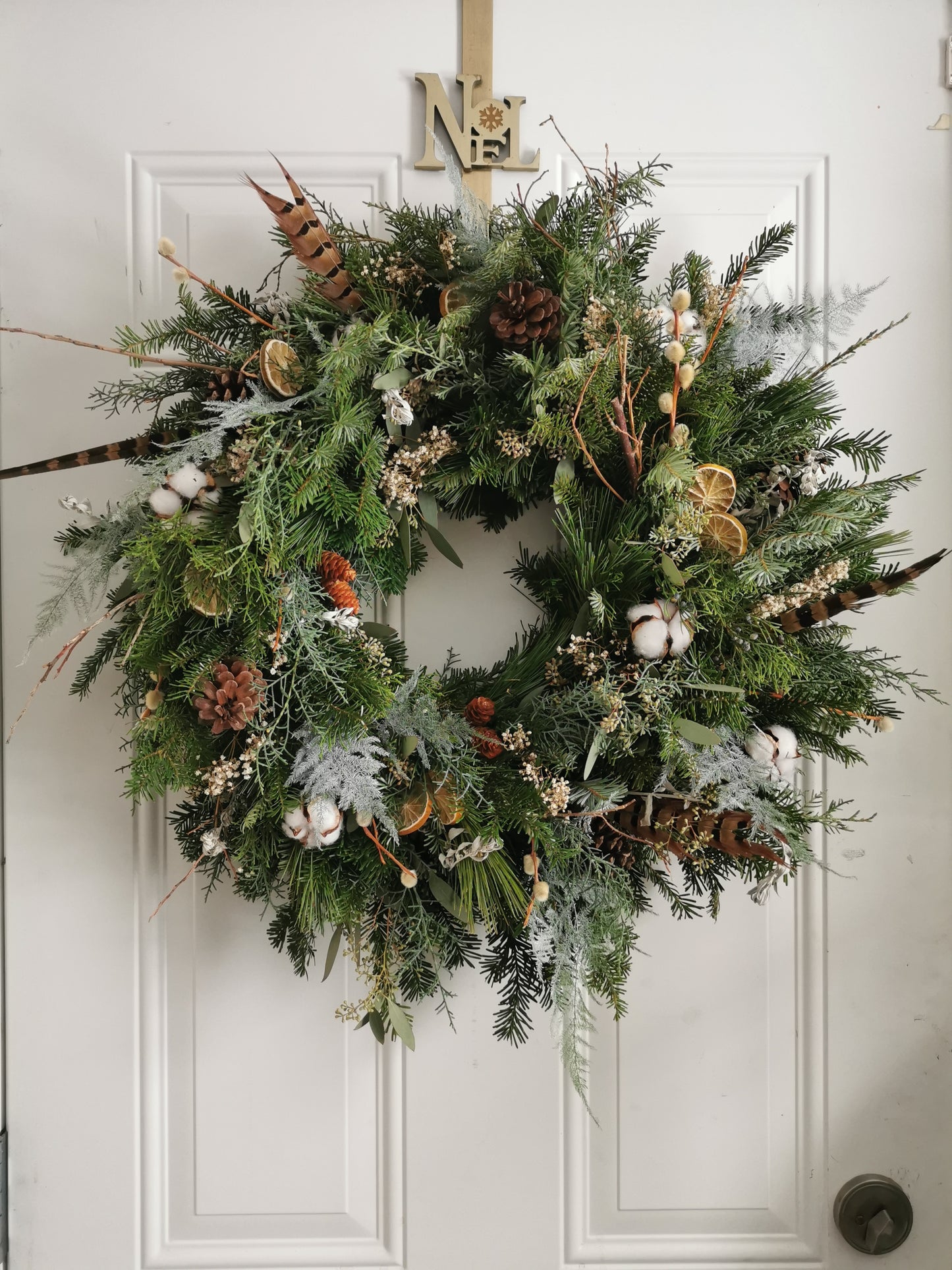 A freshly decorated Christmas wreath with a variety of greenery and dried decorations hanging on a door.